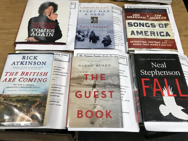 Photo of six hard cover books being recorded in January 2020 are laid out on a table. Titles are Comes Again by Howard Stern, Every Man a Hero by Ray Lambert, Songs of America by Jon Meacham & Tim McGraw, The British are Coming by Rick Atkinson, The Guest Book by Sarah Blake, and Fall by Neal Stephenson